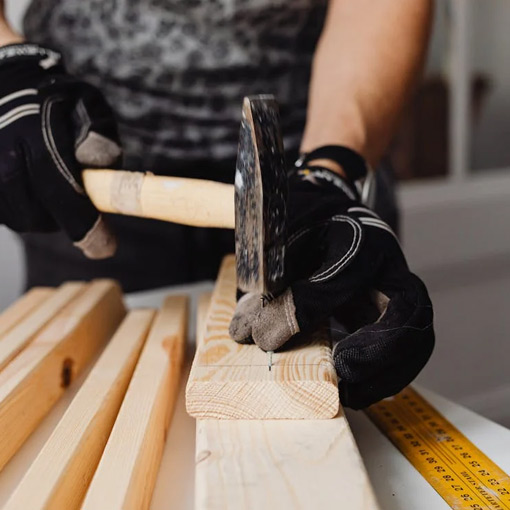 a carpentar is doing Carpentary and Joinery work with a hammer by hitting a nail in a piece of wood