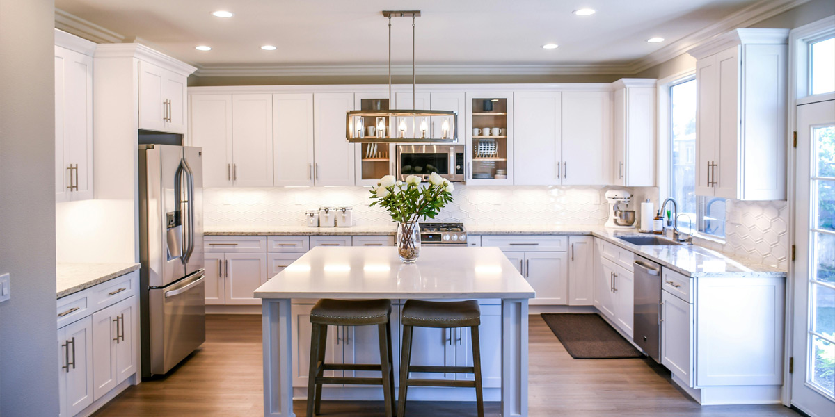 Very stylish kitchen design featuring white custom cabinets and a white marbled countertop with a small plant placed on it, complemented by two chairs underneath