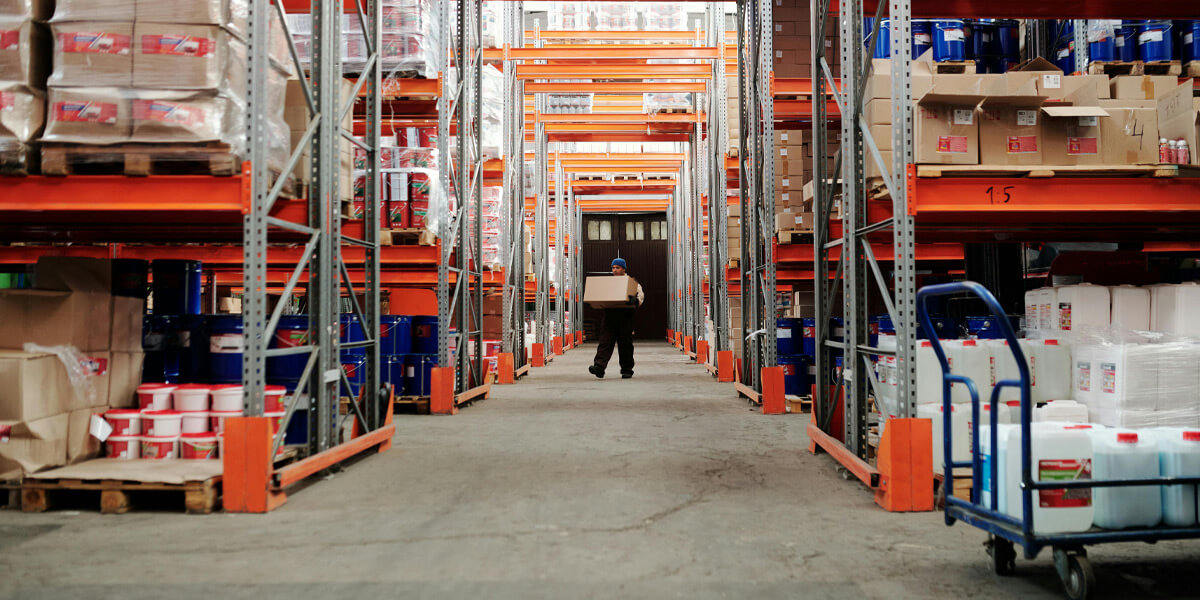 A man holding a parcel in a large warehouse interior with multiple metal shelves